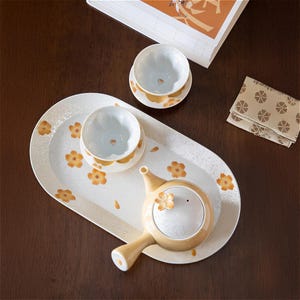 May include: A white ceramic tea set with a floral design. The set includes a teapot, two teacups, and a tray. The teapot has a small spout and a handle. The teacups have a small handle and a floral design. The tray is oval-shaped and has a floral design.