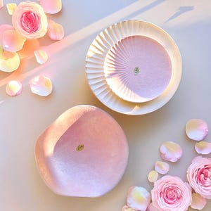 May include: Two pink ceramic plates with a textured surface. One plate is round with a fluted edge and the other is a freeform shape. Both plates have a small, round, gold sticker with Japanese characters on them.