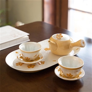 May include: A yellow ceramic teapot with a floral design on the lid, two matching teacups and saucers, and a white oval tray with a floral pattern.
