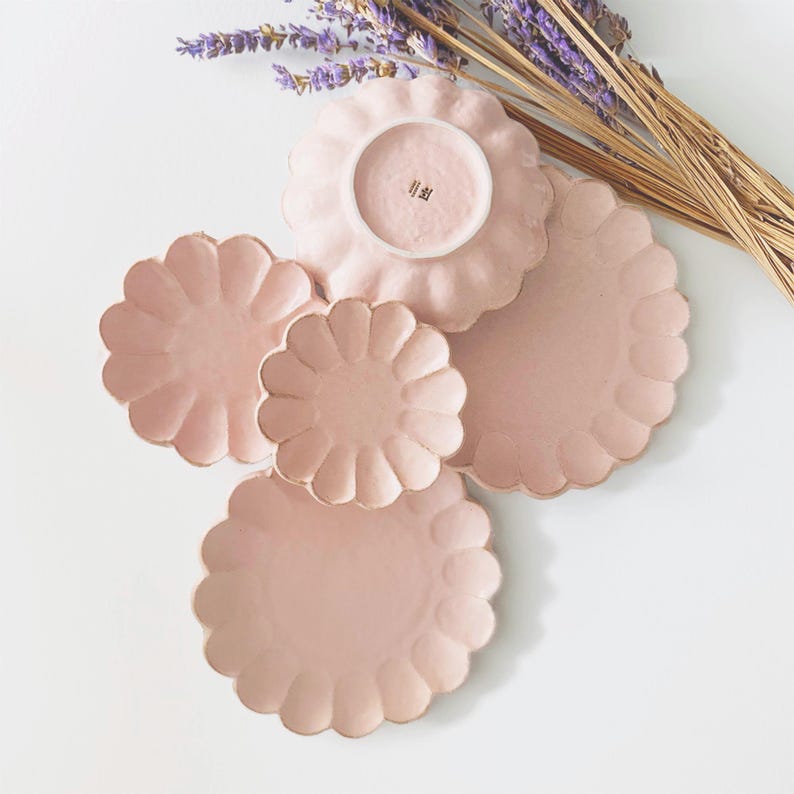 Pu&ograve; includere: Set di quattro piatti in ceramica rosa con bordi a festoni. I piatti sono impilati a forma di piramide. Il piatto pi&ugrave; piccolo ha la scritta "Hibi" sul fondo.
