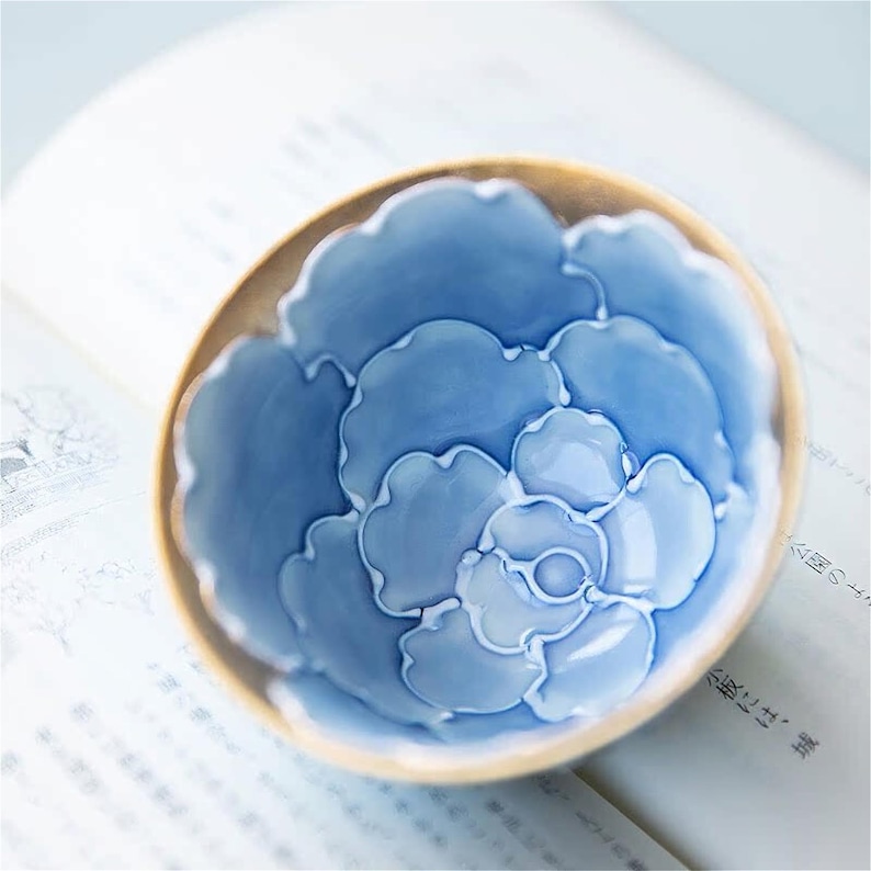 May include: A blue and white ceramic teacup with a floral design. The cup has a rounded shape and a wide rim.