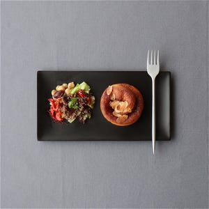 May include: A black rectangular plate holds a small salad and a pastry. The salad includes chickpeas, lettuce, and tomatoes. The pastry is topped with sliced almonds. A silver fork is placed to the right of the plate.