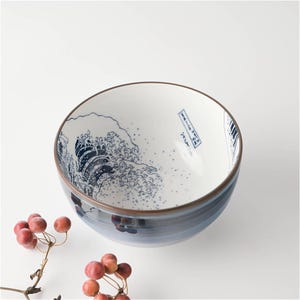May include: A white ceramic bowl with a blue and white design of a wave. The bowl has a dark blue rim and a light blue glaze.