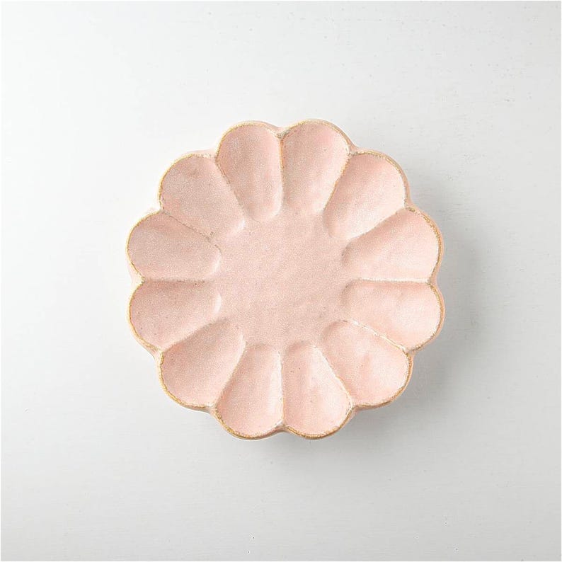Pu&ograve; includere: Un piatto in ceramica rosa pallido con un bordo ondulato e un design a forma di fiore. Il piatto &egrave; perfetto per servire piccoli spuntini o dessert.