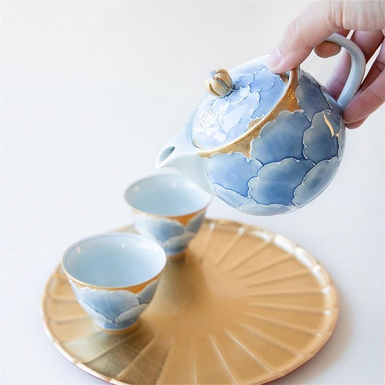 May include: A blue and gold tea set with a teapot and two cups. The teapot has a floral design and the cups have a cloud design. The set is on a gold tray.