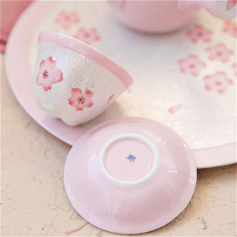 May include: A pink teacup and saucer set with a delicate floral design. The cup and saucer are decorated with white and pink cherry blossoms.