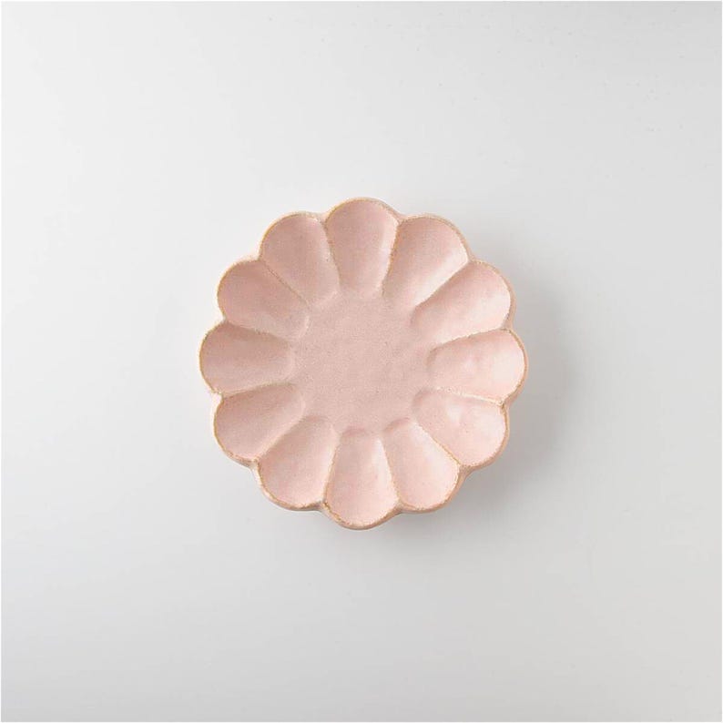 Pu&ograve; includere: Un piatto in ceramica rosa con un bordo a forma di fiore. Il piatto &egrave; perfetto per servire piccoli spuntini o dessert.