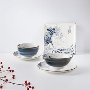 May include: Two blue and white ceramic bowls with a wave design and a matching square plate with the same design. The plate has Japanese text on it.