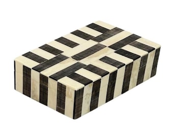 May include: Rectangular decorative box with a black and cream geometric pattern. The box features a repeating design of black and cream stripes, creating a visually appealing and symmetrical pattern. The box is likely used for storage or display.