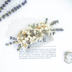 May include: A white and blue dried flower hair comb with a silver comb. The comb is on a white surface with a quote about beauty in nature.