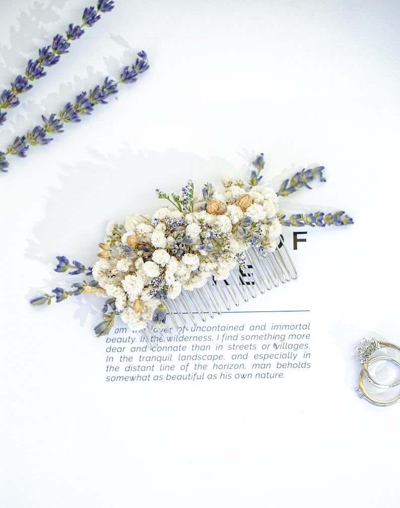May include: A white and blue dried flower hair comb with a silver comb. The comb is on a white surface with a quote about beauty in nature.