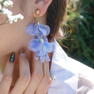 Peut inclure: Une paire de boucles d'oreilles pendantes avec une chaîne dorée et plusieurs couches de pétales de fleurs en tissu bleu clair.