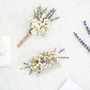 May include: Two dried flower arrangements, one a boutonniere with a brown twine wrap and the other a hair comb with white and purple flowers.
