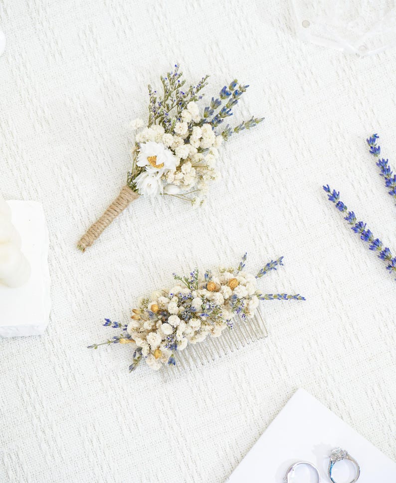 May include: Two dried flower arrangements, one a boutonniere with a brown twine wrap and the other a hair comb with white and purple flowers.