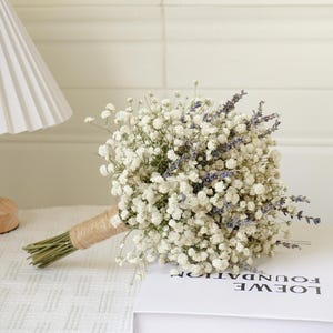 May include: A bridal bouquet made of white baby's breath and purple lavender flowers tied with twine.