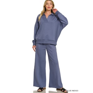 May include: A blue indigo two-piece set consisting of a long-sleeve pullover with a V-neck collar and wide-leg trousers. The pullover features dropped shoulders and a ribbed hem, while the trousers have a straight-leg cut and a clean finish.
