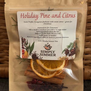 May include: A clear cellophane bag containing ingredients for a simmer pot. The label reads "Holiday Pine and Citrus." Visible ingredients include dried orange slices, cinnamon sticks, and berries. The bag also contains the text "Simply Simmer."