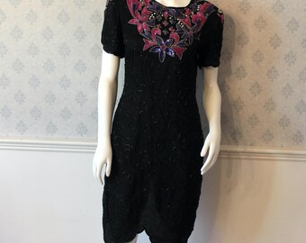 May include: A black sequined dress with a scalloped hem and a floral design on the bodice. The floral design is made of sequins in shades of pink, purple, and blue.