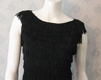 May include: A black sleeveless dress with a fringe neckline and a layered fringe design. The dress is made of a soft, flowing fabric.