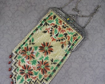 May include: Vintage metal mesh handbag with floral design in red, green, and black. The bag has a silver-tone frame and chain strap, with red bead fringe along the bottom. A classic accessory.