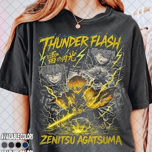 Pode incluir: T-shirt cinzenta escura com um gráfico de um personagem com cabelo amarelo e raios, com o texto "THUNDER FLASH" e "ZENITSU AGATSUMA". A camisa também mostra um design em estilo de banda desenhada com vários painéis. Disponível em cores grafite.