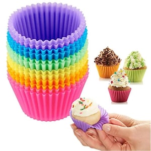 Pode incluir: Um conjunto de formas de cupcake de silicone reutilizáveis e coloridas em tons de arco-íris. A imagem também mostra cupcakes com cobertura em formas laranja, verdes e vermelhas, com um cupcake sendo segurado em uma forma roxa.