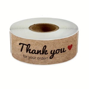 May include: A roll of brown kraft paper stickers with the words "Thank you for your order!" in black script and a red heart. The stickers are designed for packaging and include a white backing.