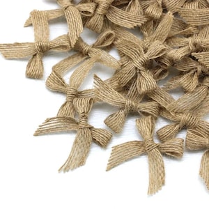 May include: A collection of small, rustic jute twine bows. The bows are tied with a simple knot in the centre and have a textured appearance. They are scattered on a white surface, suggesting a craft or decorative theme, ideal for embellishments.