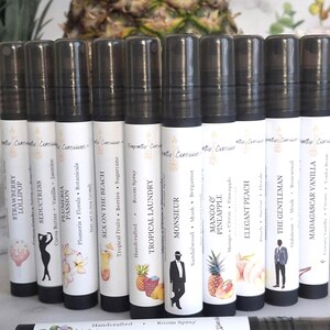 Puede incluir: Una colecci&oacute;n de diez aerosoles ambientales cil&iacute;ndricos con tapas negras y etiquetas blancas. Cada etiqueta presenta un dise&ntilde;o &uacute;nico y un nombre de aroma, como "Tropical Laundry" y "Mango & Pineapple". El aerosol inferior dice "Fragrant Botanicals".
