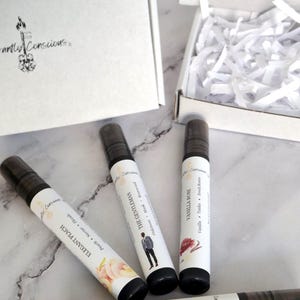 Puede incluir: Se muestran cuatro botellas de spray ambiental con tapas negras y etiquetas blancas. Las etiquetas dicen "Elegant Peach", "The Gentleman", "Vanilla Rose" y "Sex on the Beach". Una caja blanca y papel triturado est&aacute;n en el fondo.