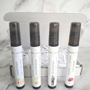 Puede incluir: Cuatro botellas de spray ambiental con tapas negras y etiquetas blancas dentro de una caja blanca. Las etiquetas dicen "Elegant Peach", "Sex on the Beach", "The Gentleman" y "Vanilla Rose". La caja est&aacute; sobre una superficie con vetas de m&aacute;rmol.