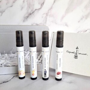 Puede incluir: Cuatro frascos de spray de perfume con tapas negras y etiquetas blancas, cada uno con un nombre de aroma diferente: Elegant Peach, Sex on the Beach, The Gentleman y Vanilla Rose. Los frascos est&aacute;n frente a una caja blanca.