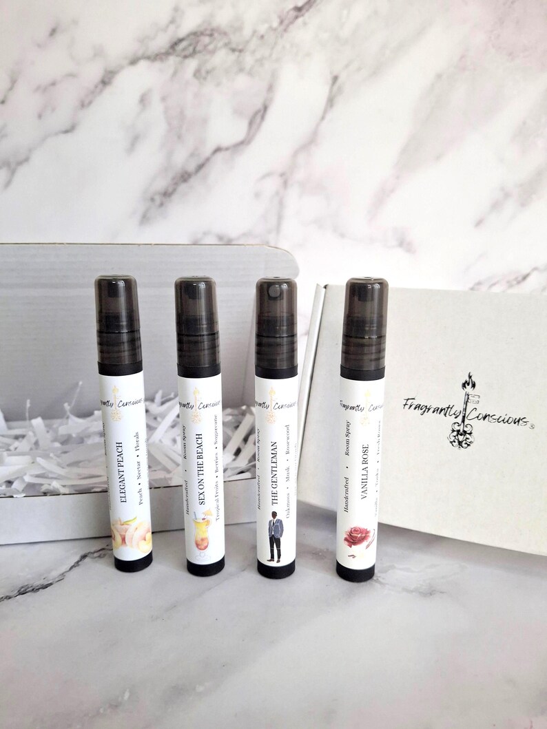 Puede incluir: Cuatro frascos de spray de perfume con tapas negras y etiquetas blancas, cada uno con un nombre de aroma diferente: Elegant Peach, Sex on the Beach, The Gentleman y Vanilla Rose. Los frascos est&aacute;n frente a una caja blanca.