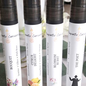 Puede incluir: Cuatro botellas de spray ambiental con tapas negras y etiquetas blancas. Las etiquetas presentan el texto "Fragrant Conscious" y los nombres "Bouquet", "Citrus Delight", "Blossom Burst" y "The Poet". Cada etiqueta tiene un dise&ntilde;o floral o gr&aacute;fico &uacute;nico.