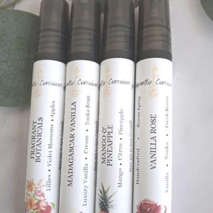 Puede incluir: Se muestran cuatro botellas de spray blancas con tapas negras. Cada botella tiene una etiqueta con texto e ilustraciones. Las etiquetas dicen: Fragrant Botanicals, Madagascar Vanilla, Mango & Pineapple y Vanilla Rose. Cada botella contiene 10 ml.