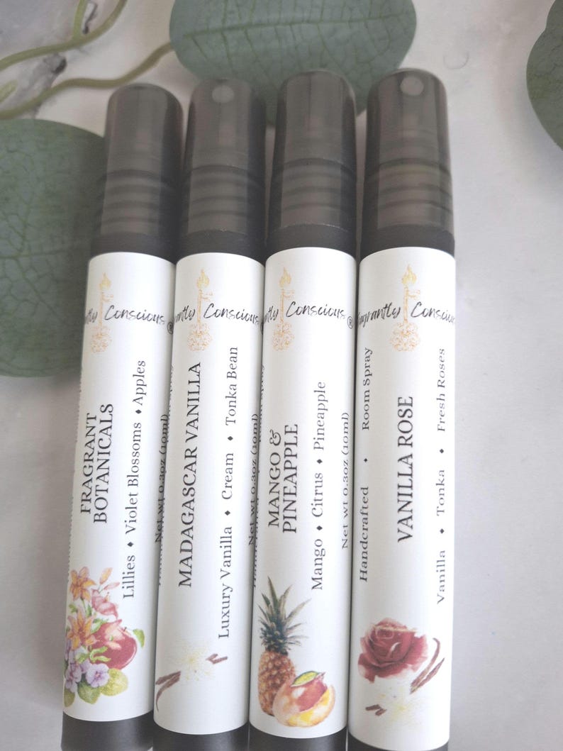Puede incluir: Se muestran cuatro botellas de spray blancas con tapas negras. Cada botella tiene una etiqueta con texto e ilustraciones. Las etiquetas dicen: Fragrant Botanicals, Madagascar Vanilla, Mango & Pineapple y Vanilla Rose. Cada botella contiene 10 ml.