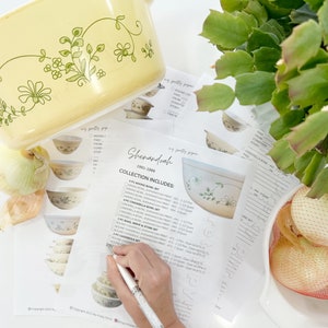 Puede incluir: Un primer plano de una hoja de papel blanca con una lista de artículos de cocina Shenandoah, que incluyen tazones para mezclar, platos para hornear y utensilios para hornear. La lista incluye el tamaño y la impresión de cada artículo. Una mano sostiene un bolígrafo y apunta a la lista.