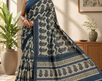 May include: A saree featuring a cream-coloured base with a repeating dark blue paisley print. The garment includes a wide border with intricate horizontal stripes and a matching dark blue blouse, draped to showcase the detailed textile pattern.