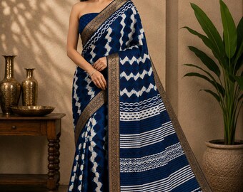 May include: A deep blue and white saree featuring a repeating zigzag and geometric pattern throughout the fabric. The garment is finished with a wide, ornate metallic gold border that runs along the edges, providing a distinct contrast to the blue.
