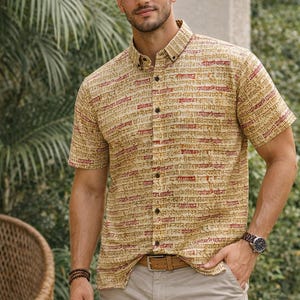 May include: A short-sleeved button-down shirt with a beige background and red script print. The shirt is paired with khaki shorts and a brown belt. A watch and bracelets are also visible.
