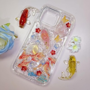 May include: Clear phone case with embedded koi fish, flowers, and butterflies. The case features red, pink, and gold fish, with red, blue, and white floral accents. Two additional koi fish are placed near the case.