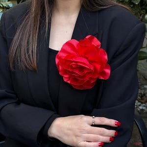 May include: A large, red satin flower brooch pinned to a black blazer.