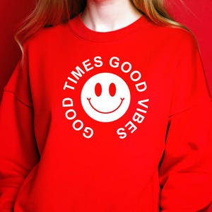 May include: A red sweatshirt with a white smiley face graphic and the words "GOOD TIMES GOOD VIBES" in a circular design. The sweatshirt is a solid red color and has long sleeves.