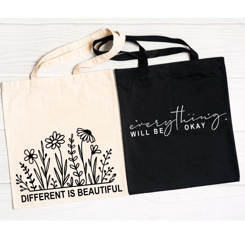 Pu&ograve; includere: Due borse tote, una nera e una beige. La borsa nera ha un testo bianco che dice "tutto andr&agrave; bene". La borsa beige ha un testo nero che dice "diverso &egrave; bello" e un disegno a linea nera di fiori.