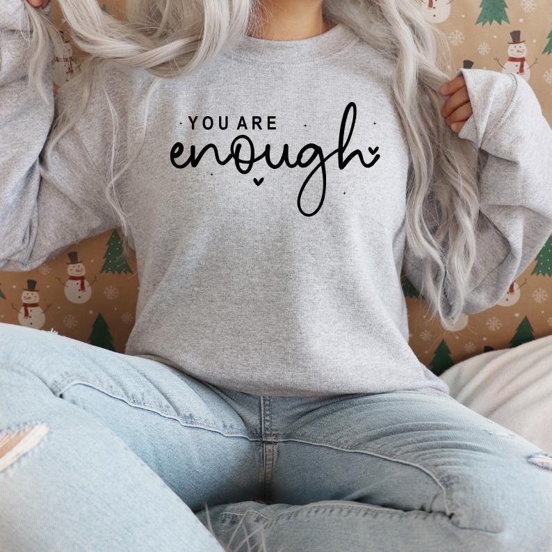 Pu&ograve; includere: Una felpa grigia con il testo "You are enough" in lettere corsive nere.