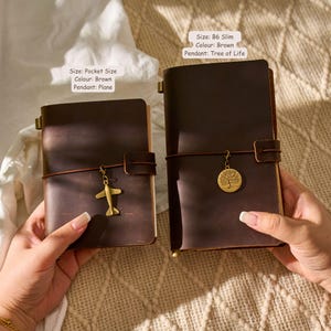 May include: Two brown leather journals, one pocket-sized with a plane charm and the other B6 slim with a Tree of Life pendant. The text on the image reads "Size: Pocket Size, Colour: Brown, Pendant: Plane" and "Size: B6 Slim, Colour: Brown, Pendant: Tree of Life."