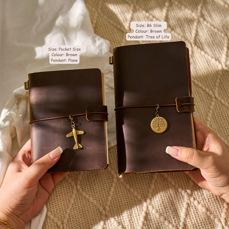 May include: Two brown leather journals, one pocket-sized with a plane charm and the other B6 slim with a Tree of Life pendant. The text on the image reads "Size: Pocket Size, Colour: Brown, Pendant: Plane" and "Size: B6 Slim, Colour: Brown, Pendant: Tree of Life."