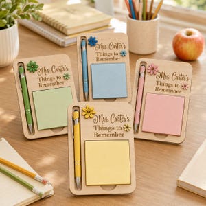 Peut inclure: Trois porte-notes en bois avec le texte "Mrs. Carter's Things to Remember" gravé sur le devant. Chaque support comprend un stylo dans une fente latérale et un bloc de notes adhésives carré vert, bleu ou rose, orné d'une petite fleur en bois.