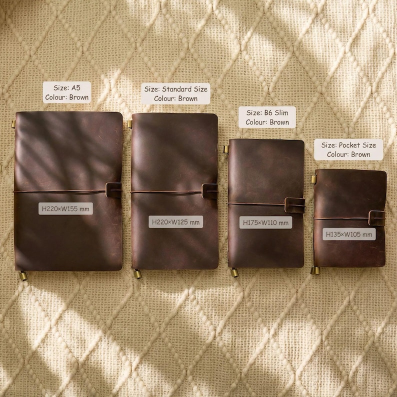 May include: Four brown leather journals of varying sizes are displayed, each with a brass clasp and closure. The sizes are A5, Standard, B6 Slim, and Pocket, with dimensions in millimeters. The journals are arranged on a textured, beige surface.