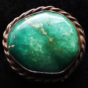May include: A turquoise stone ring with a silver setting. The stone is a bright green colour with white veins running through it. The setting is a twisted rope design.